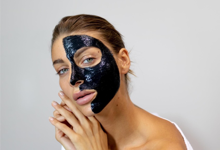Jeune femme appliquant un masque de peeling au carbone sur la moitié de son visage.