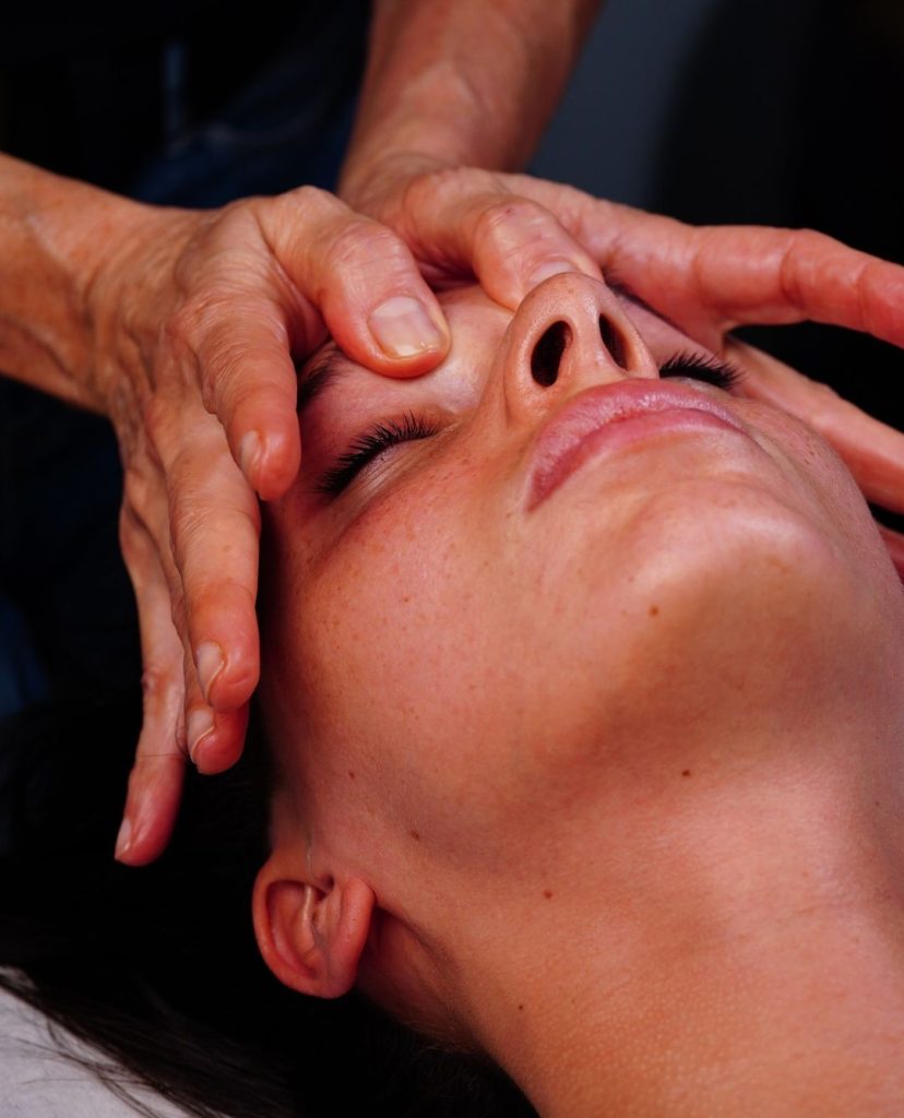 Une femme en séance de massage du visage, avec la masseuse prenant soin de son visage.